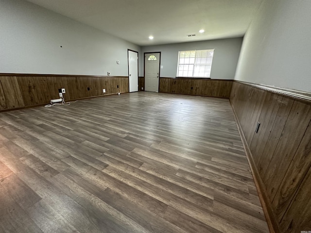 empty room with dark wood-type flooring, wooden walls, visible vents, and a wainscoted wall