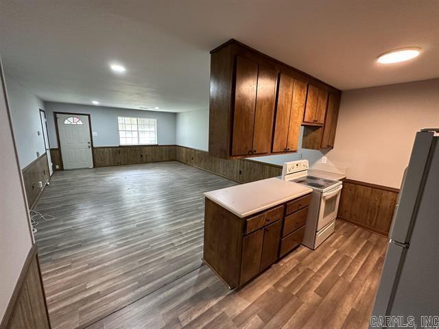 kitchen with white electric range, wooden walls, wood finished floors, freestanding refrigerator, and wainscoting