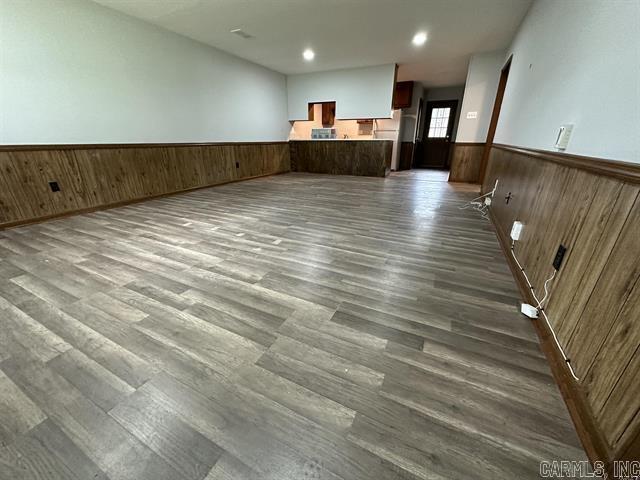 unfurnished living room with dark wood finished floors, wood walls, a wainscoted wall, and recessed lighting
