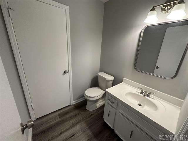 half bath with wood finished floors, vanity, and toilet