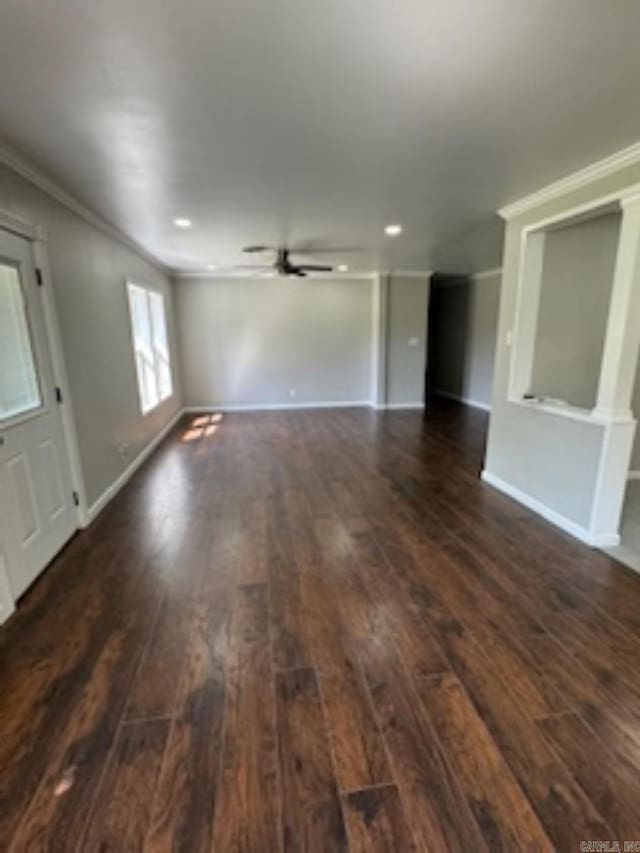 unfurnished living room featuring dark wood-type flooring, crown molding, a ceiling fan, and baseboards