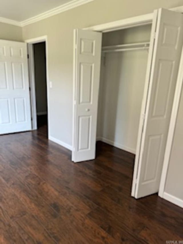 unfurnished bedroom featuring baseboards, a closet, ornamental molding, and dark wood finished floors