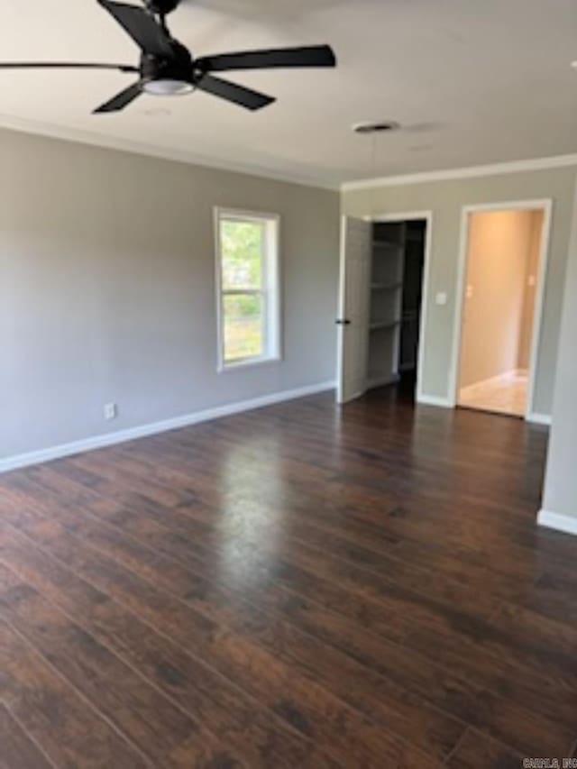 empty room featuring a ceiling fan, baseboards, dark wood-type flooring, and crown molding