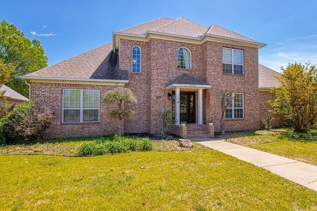 view of front of property featuring roof with shingles, brick siding, and a front yard