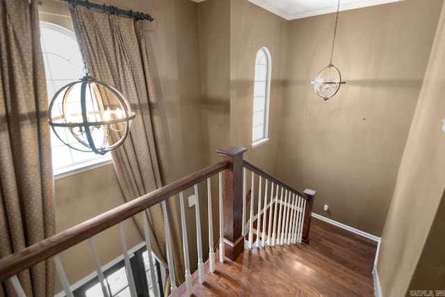 stairs with baseboards, ornamental molding, an inviting chandelier, and wood finished floors