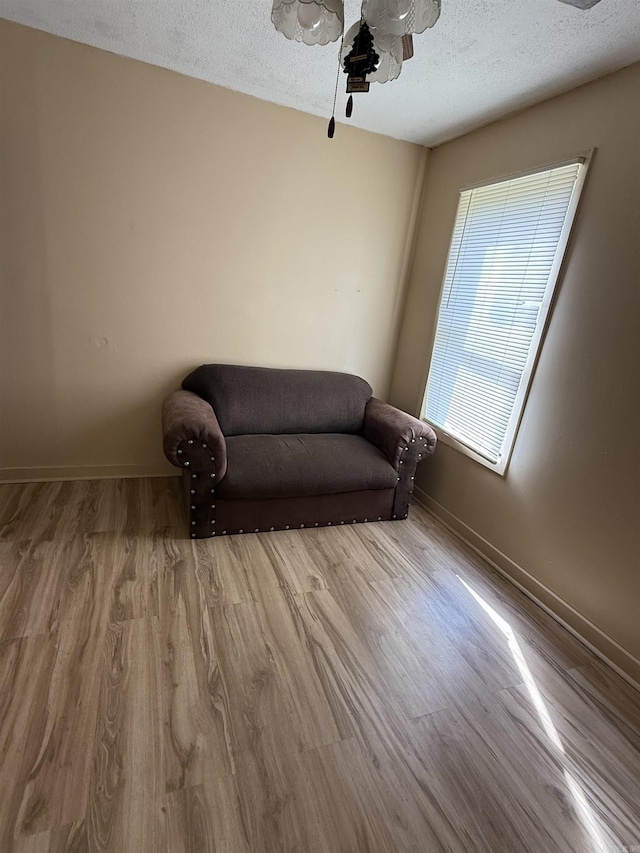 living area featuring baseboards, a ceiling fan, wood finished floors, and a textured ceiling