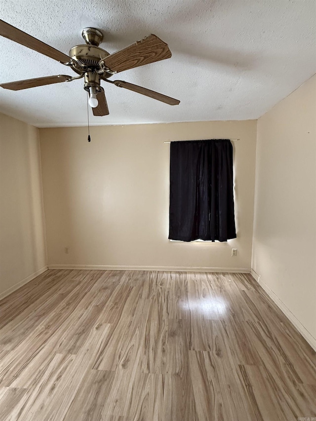 spare room featuring light wood-type flooring, a textured ceiling, a ceiling fan, and baseboards