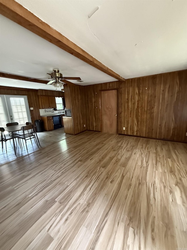 unfurnished living room with a ceiling fan, beamed ceiling, light wood finished floors, and wooden walls