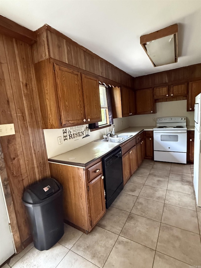 kitchen featuring brown cabinets, wooden walls, a sink, light tile patterned flooring, and white appliances