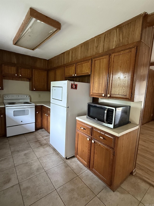 kitchen featuring brown cabinetry, light tile patterned floors, white appliances, and light countertops