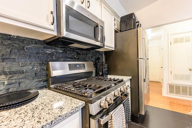kitchen with white cabinets, visible vents, decorative backsplash, dark tile patterned floors, and appliances with stainless steel finishes