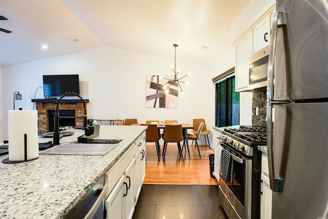 kitchen with vaulted ceiling, white cabinetry, stainless steel appliances, and dark tile patterned flooring