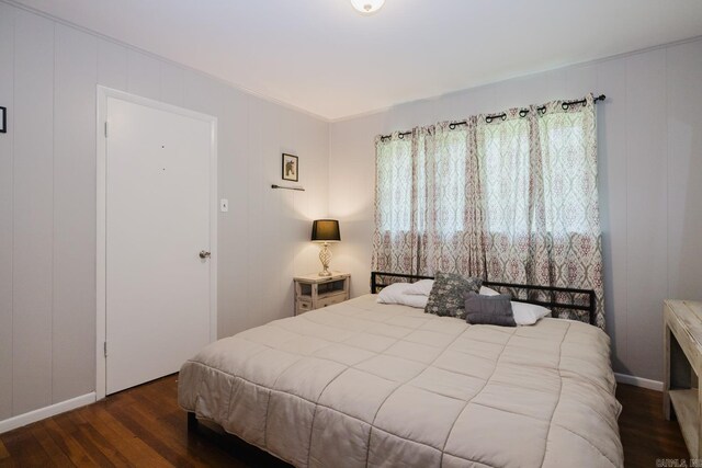 bedroom featuring baseboards, wood finished floors, and a decorative wall