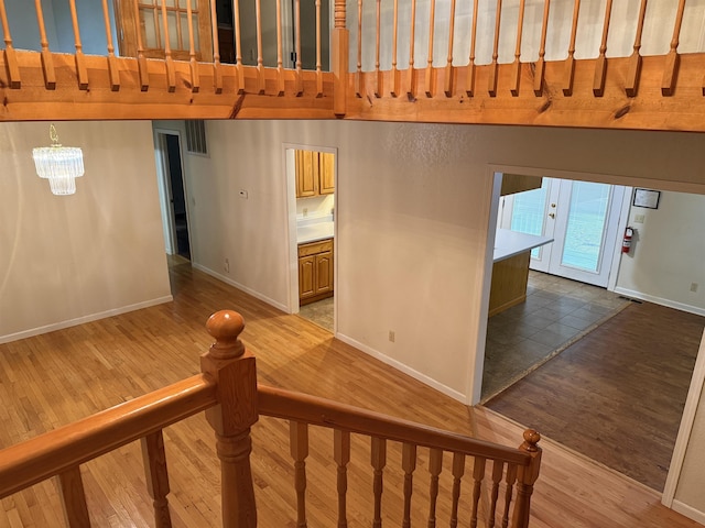 stairway with wood finished floors, a high ceiling, baseboards, and a notable chandelier