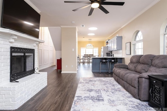 living room with ceiling fan, a fireplace, baseboards, ornamental molding, and dark wood-style floors