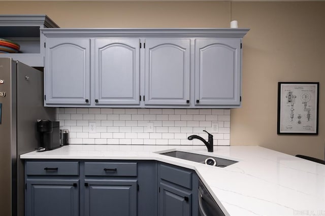 kitchen with stainless steel appliances, a sink, decorative backsplash, gray cabinetry, and light stone countertops