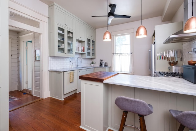 kitchen with backsplash, a sink, dark wood-type flooring, and wall chimney range hood