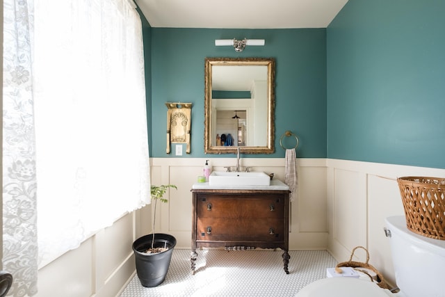 bathroom featuring a decorative wall, toilet, vanity, and wainscoting