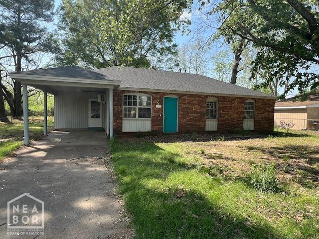 ranch-style home featuring driveway, an attached carport, and a front yard