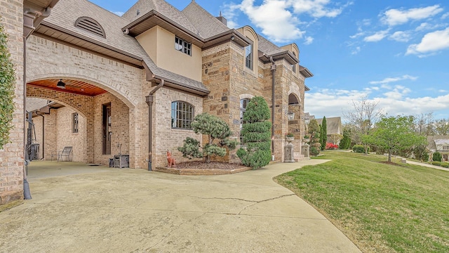 exterior space featuring a high end roof, driveway, stone siding, a yard, and brick siding