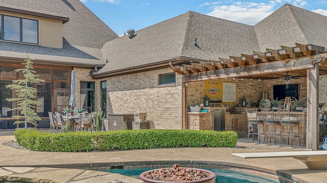 rear view of property with a fire pit, outdoor dry bar, brick siding, and a shingled roof