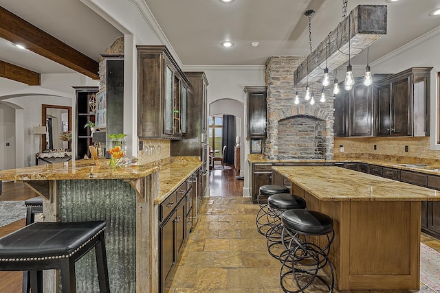 kitchen with arched walkways, a kitchen bar, light stone counters, and tasteful backsplash