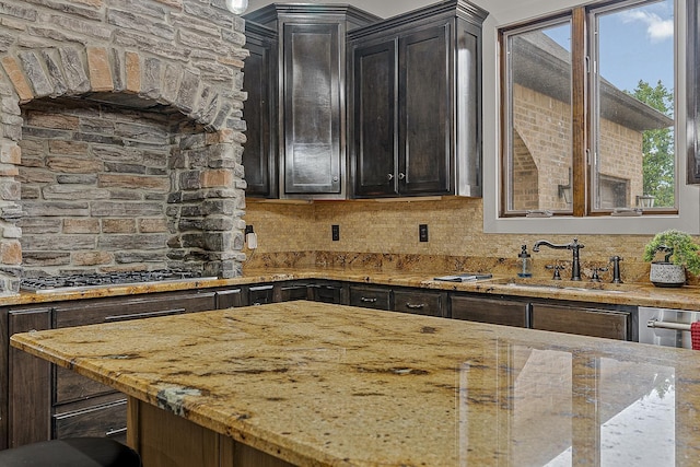 kitchen with stainless steel gas stovetop, backsplash, light stone countertops, and a sink