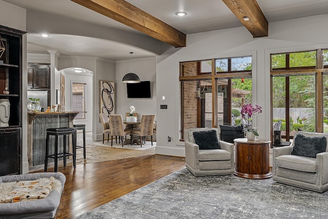 living room with arched walkways, wood finished floors, beamed ceiling, and plenty of natural light