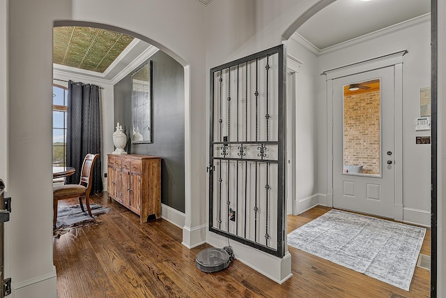 entrance foyer featuring baseboards, wood finished floors, arched walkways, and crown molding