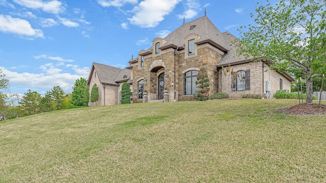 french country home featuring brick siding, stone siding, and a front yard