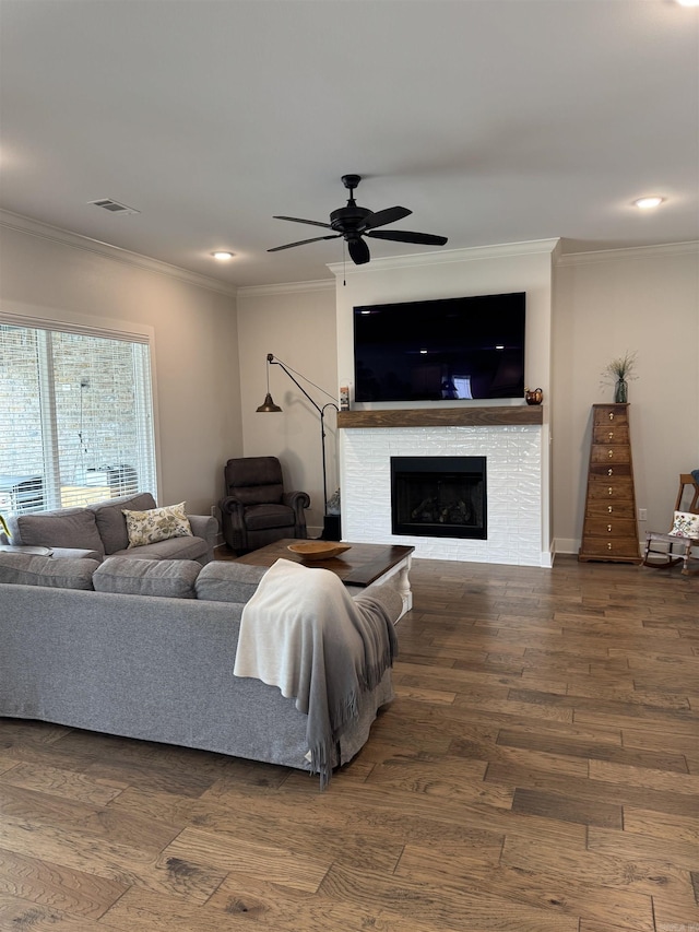 living area featuring a ceiling fan, crown molding, wood finished floors, a tile fireplace, and visible vents