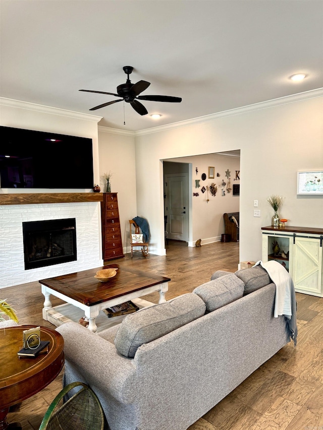 living room featuring wood finished floors, a ceiling fan, crown molding, baseboards, and a fireplace