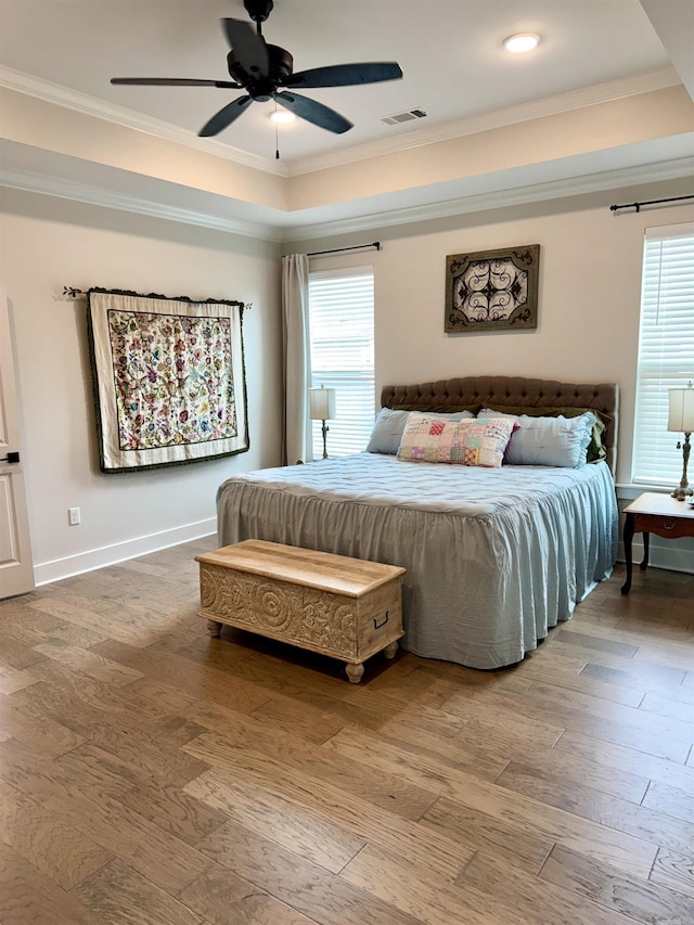 bedroom with a raised ceiling, visible vents, crown molding, and multiple windows