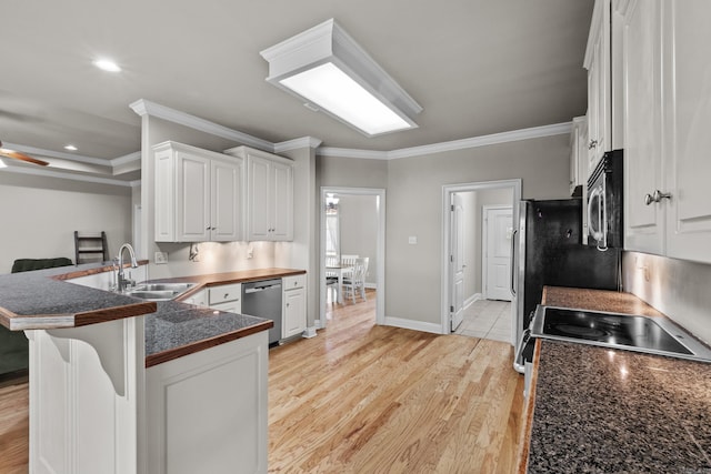 kitchen featuring dark countertops, crown molding, stainless steel appliances, light wood-style flooring, and white cabinets