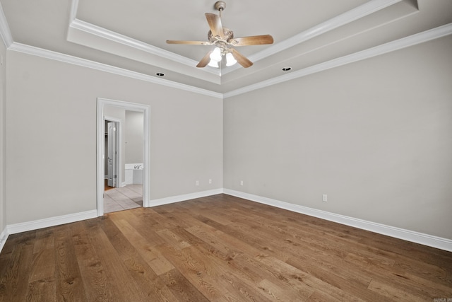 empty room with a raised ceiling, baseboards, a ceiling fan, wood finished floors, and ornamental molding