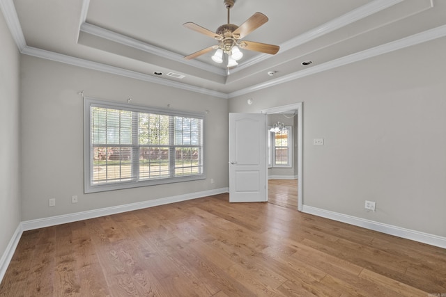 spare room with a tray ceiling, ornamental molding, light wood-type flooring, baseboards, and ceiling fan