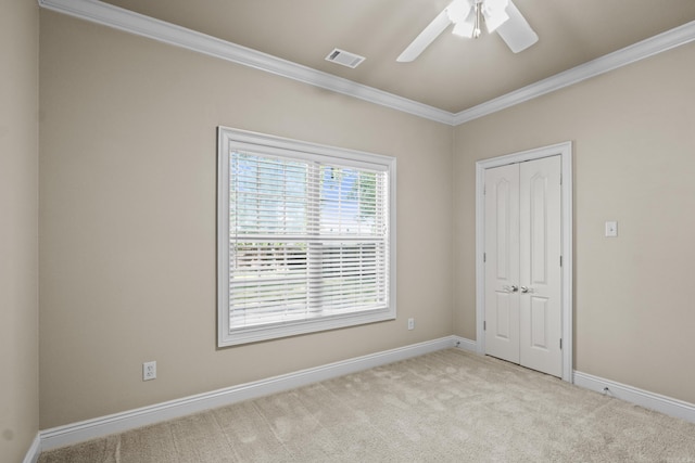 carpeted spare room featuring ceiling fan, baseboards, ornamental molding, and visible vents
