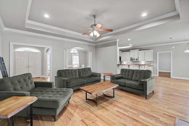 living room featuring a ceiling fan, light wood-style floors, arched walkways, a raised ceiling, and baseboards