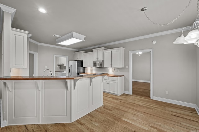 kitchen featuring a kitchen breakfast bar, stainless steel appliances, ornamental molding, a peninsula, and white cabinetry