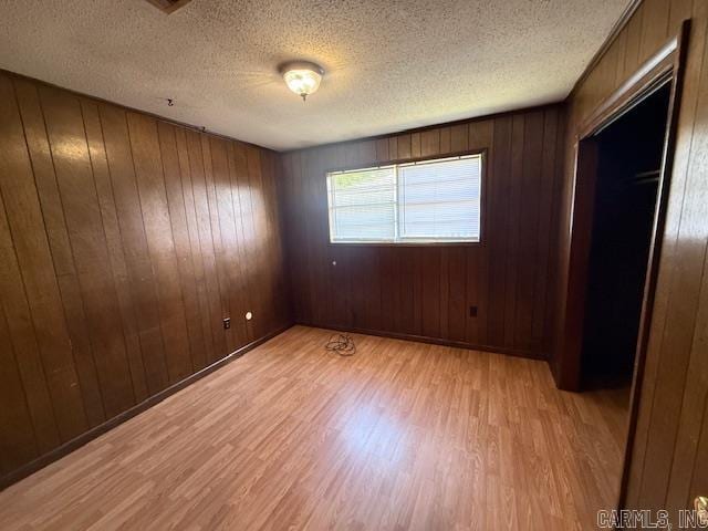 unfurnished bedroom featuring light wood-style flooring, wooden walls, and a textured ceiling