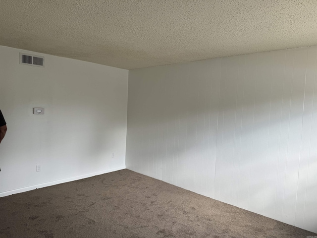 unfurnished room with dark colored carpet, visible vents, and a textured ceiling