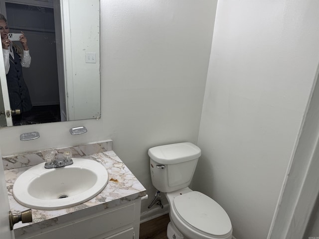 half bathroom with baseboards, toilet, and vanity