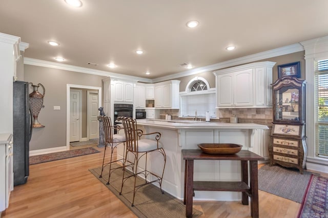 kitchen featuring white cabinets, ornamental molding, decorative backsplash, black appliances, and a kitchen bar