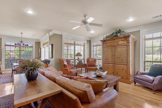 living area with a wealth of natural light, ceiling fan with notable chandelier, visible vents, and light wood-type flooring