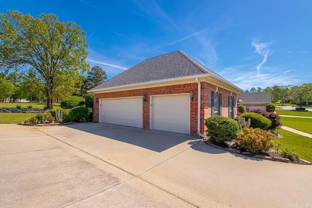 view of side of property featuring concrete driveway, a lawn, a shingled roof, an attached garage, and brick siding