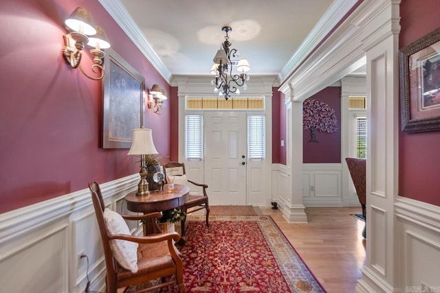 foyer entrance featuring light wood-style flooring, a decorative wall, crown molding, and ornate columns
