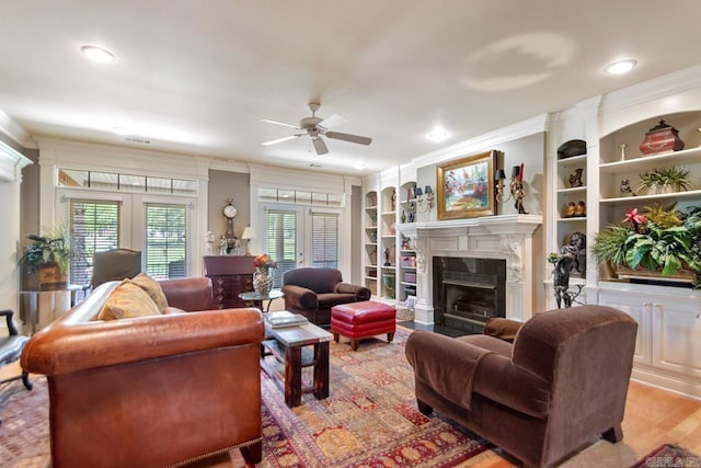 living area with a ceiling fan, crown molding, built in shelves, french doors, and a fireplace