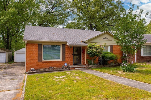 view of front of house with a shingled roof, a front lawn, an outdoor structure, and brick siding