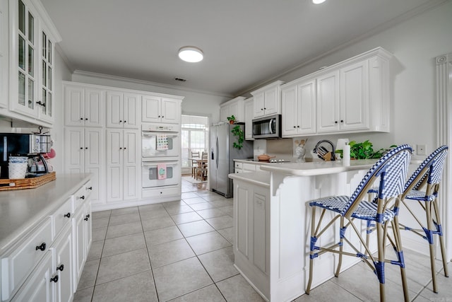 kitchen featuring stainless steel appliances, crown molding, a kitchen bar, glass insert cabinets, and white cabinetry