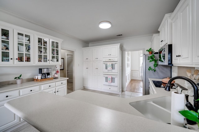 kitchen with crown molding, a sink, glass insert cabinets, white cabinets, and appliances with stainless steel finishes